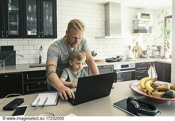 Father and son using laptop in kitchen