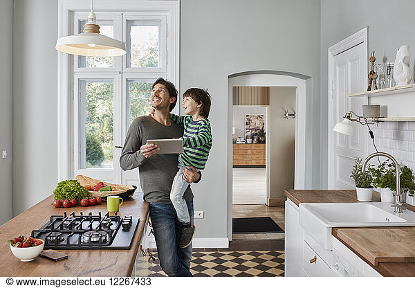 Father and son using tablet in kitchen looking at ceiling lamp