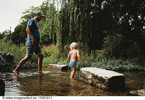 Father and son walking in the water in stream in summer