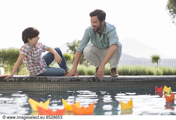 Father and son watching origami boats in swimming pool