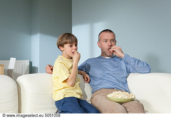 Father and son watching television eating popcorn