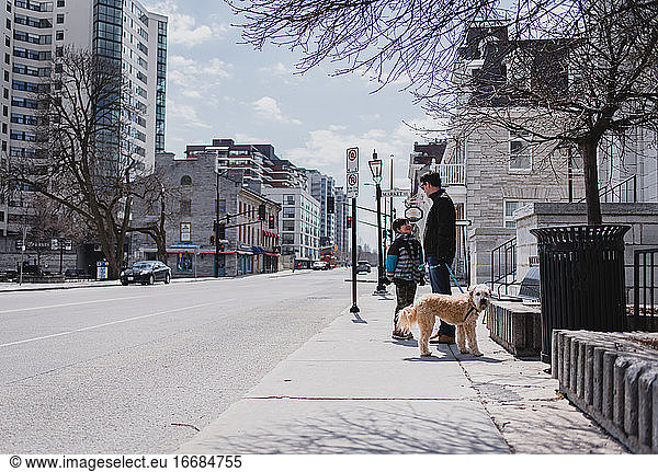 Father and son with dog standing on sidewalk of a quiet city street.