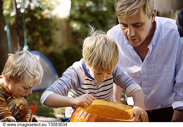 Father and sons carving pumpkin for Halloween at yard