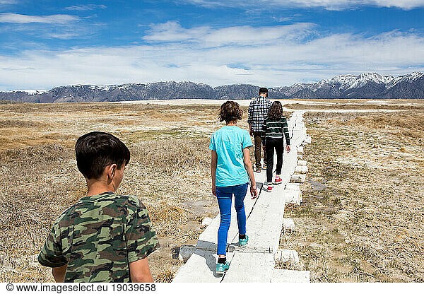 Father and three children walk on a boarded path toward the mountains