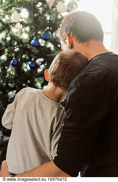 Father and toddler hugging by Christmas tree sharing tender moment