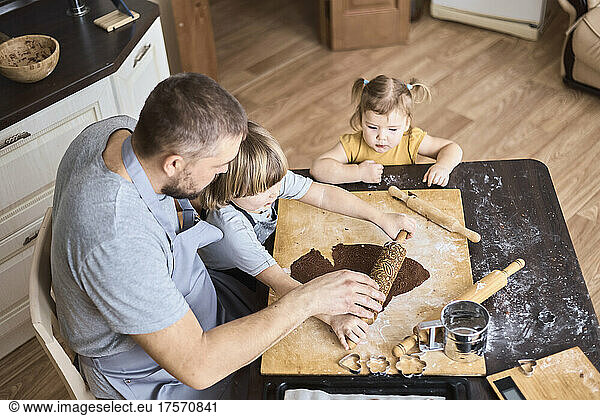 Father and two children rolling out chocolate cookie dough