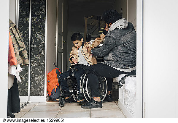 Father assisting disabled son in getting dressed at doorway