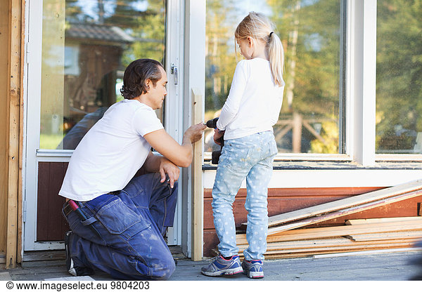 Father assisting girl in using cordless screwdriver on frame during home improvement