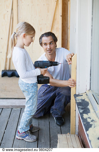 Father assisting girl in using cordless screwdriver while home improving