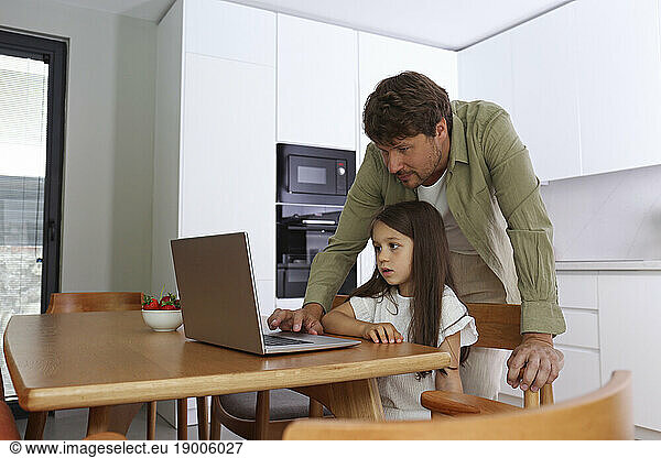 Father assisting girl using laptop at home