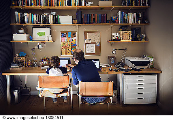 Father assisting son in using laptop computer at home