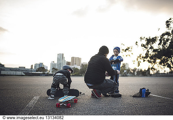 Father assisting sons in preparation for skateboarding at field