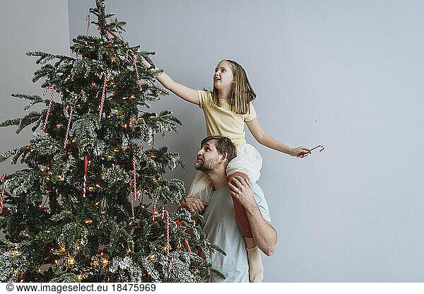 Father carrying daughter on shoulders for decorating Christmas tree at home