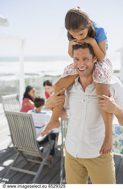 Father carrying daughter on shoulders on sunny patio