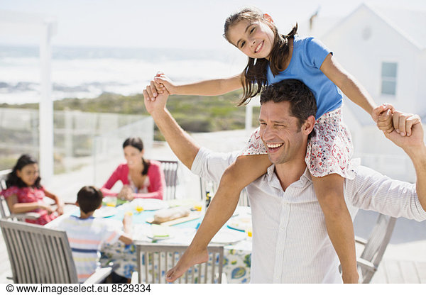 Father carrying daughter on shoulders on sunny patio
