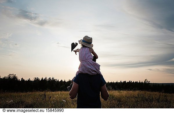 father carrying his daughter on his shoulders in a meadow at sunset