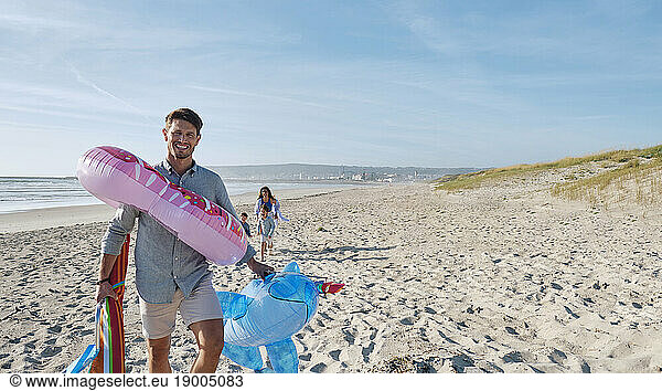 Father carrying inflatable swim rings at beach on sunny day