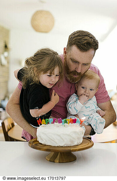 Father carrying kids (2-3  6-11 months) and blowing birthday candles on cake