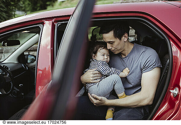 Father carrying male toddler while sitting in car