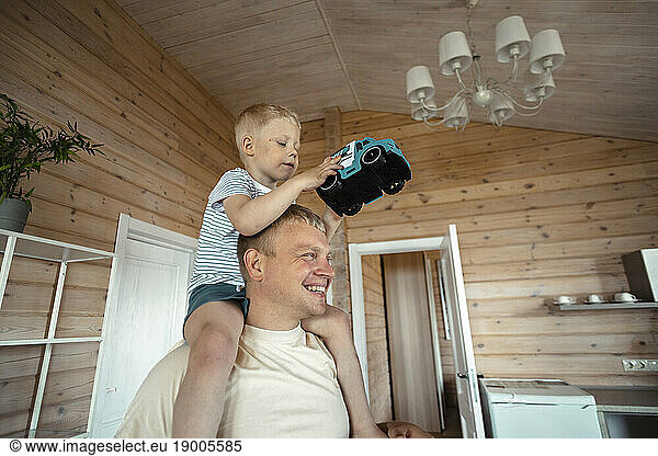 Father carrying playful son on shoulders at home