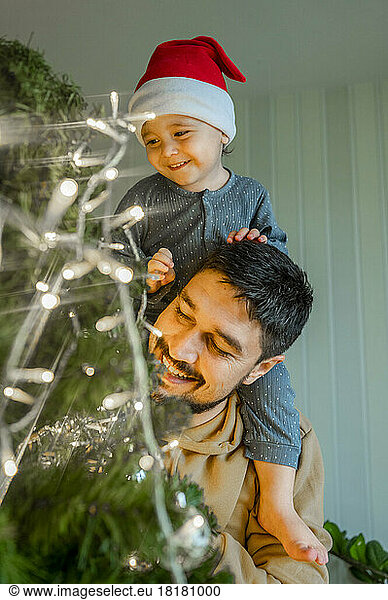 Father carrying son and decorating Christmas tree at home