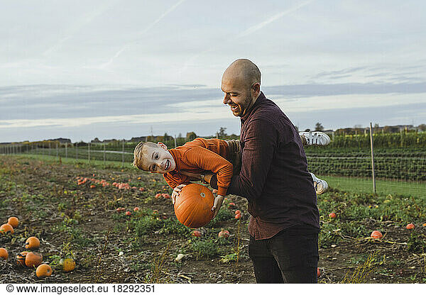 Father carrying son holding pumpkin in field