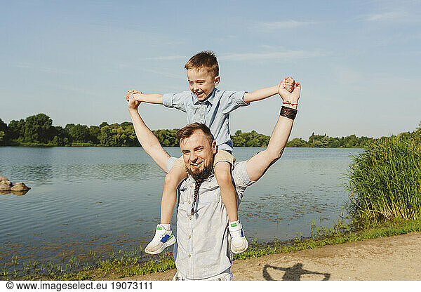 Father carrying son on shoulder at lakeshore