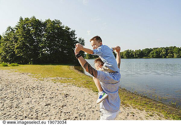 Father carrying son on shoulder by lake