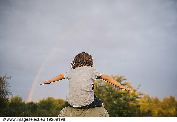 Father carrying son on shoulders under sky at sunset