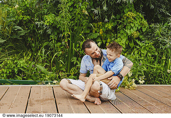 Father carrying son sitting on footbridge in front of plants