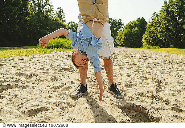 Father carrying son upside down on field