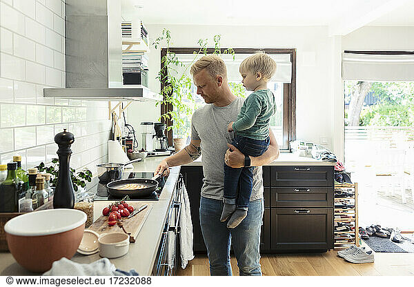 Father carrying son while cooking food in kitchen