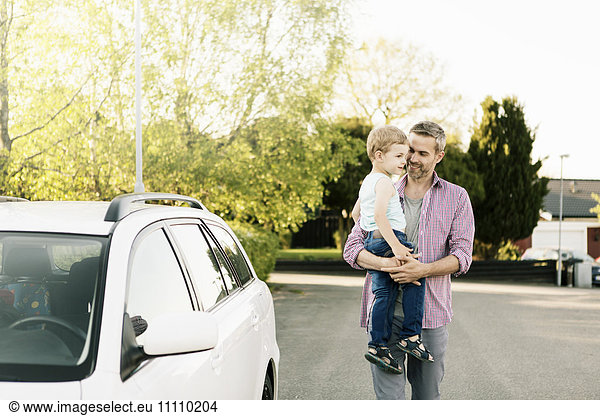 Father carrying son while walking by car on street
