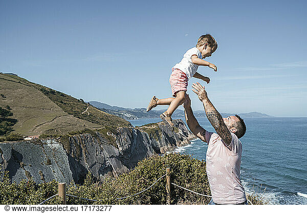 Father catching son at observation point against blue sky on sunny day
