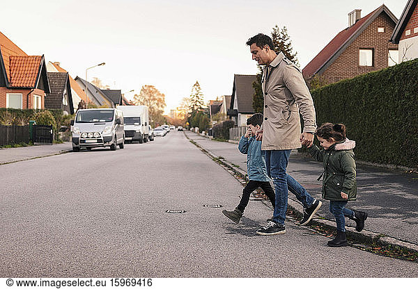 Father crossing footpath with children during autumn