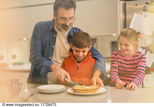 Father cutting and serving pie to children in kitchen