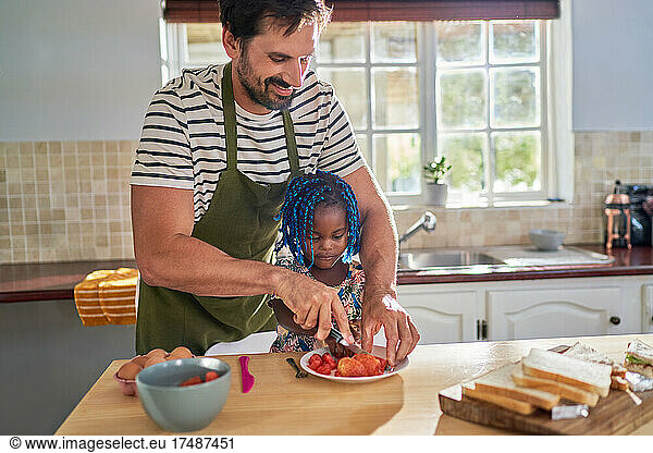 Father cutting fruit for toddler daughter in kitchen