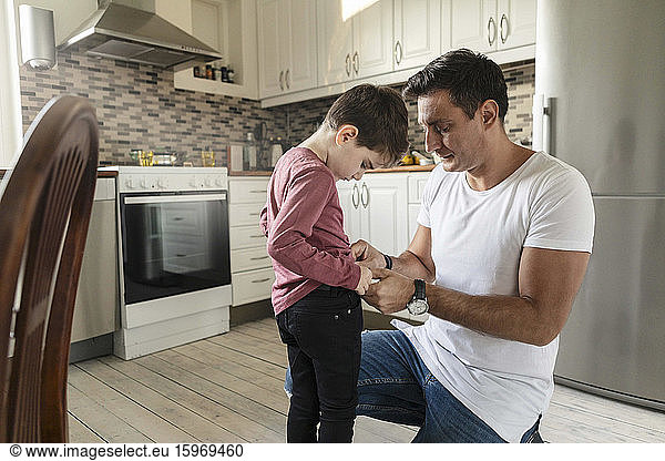Father dressing up son while kneeling on kitchen floor