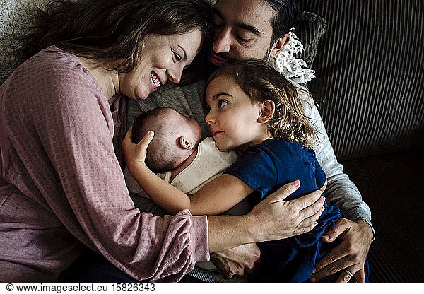 Father embraces family as mother smiles at 4 yr old and newborn
