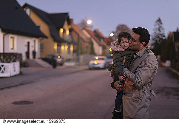 Father embracing and kissing sad daughter while standing outdoors during sunset
