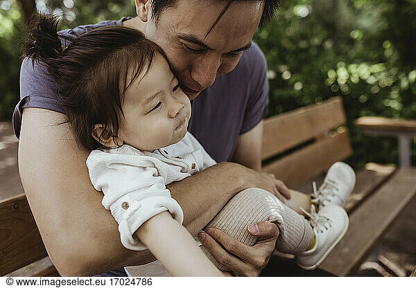 Father embracing male toddler while sitting on bench