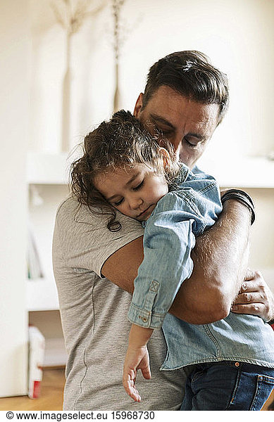 Father embracing sad daughter while standing at home