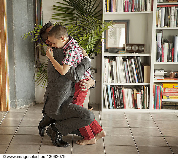Father embracing son by bookshelf in living room
