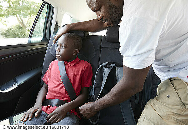 Father fastening seat belt for son in back seat of car