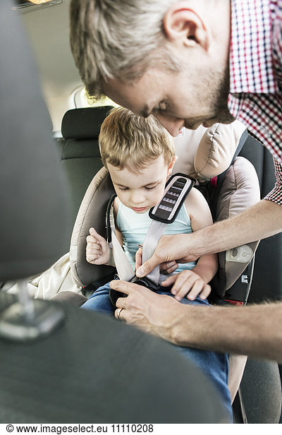 Father fastening seat belt for son in car