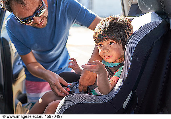 Father fastening son in car seat