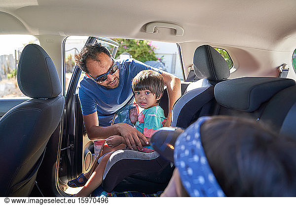 Father fastening toddler son into car seat