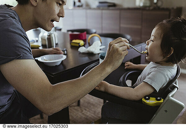 Father feeding food to baby son in kitchen