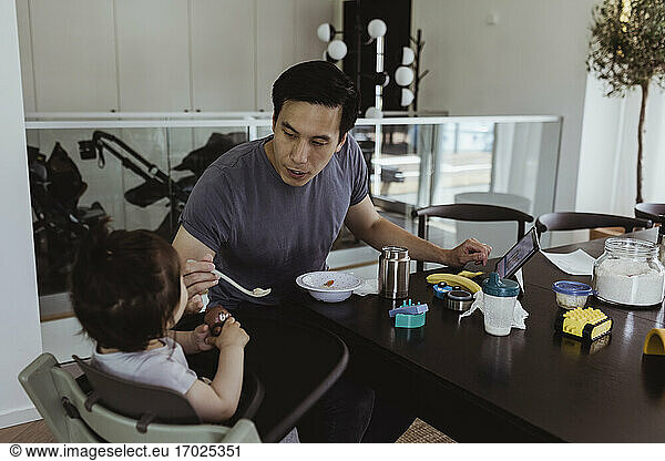 Father feeding male toddler over table at home