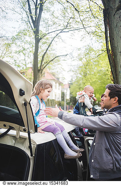 Father gesturing towards girl sitting on car